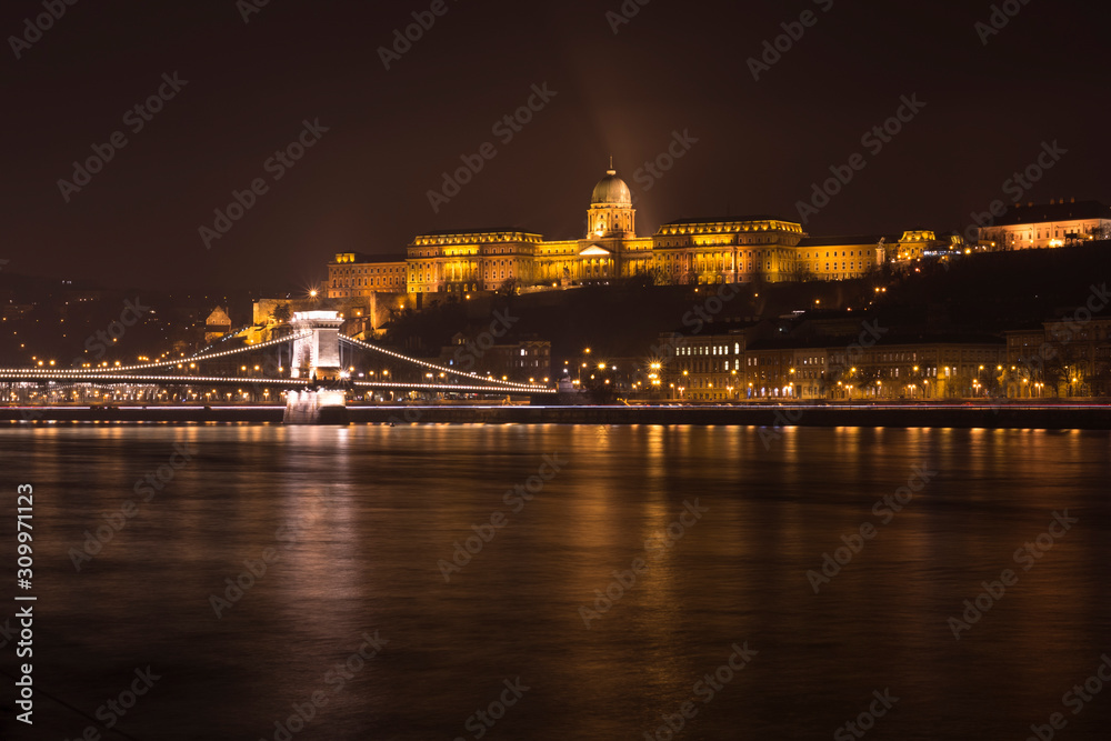 Night view through Danube on Buda castle and Matyas cathedral. City Budapest at night. Illuminated Buda castle and Matyas cathedral.