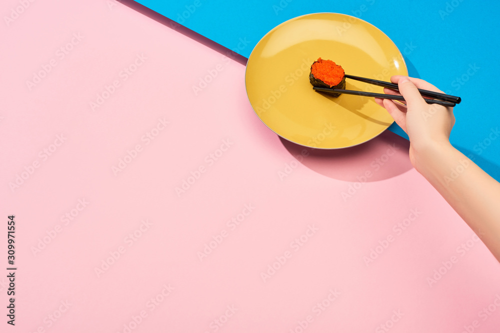 cropped view of woman eating fresh nigiri with red caviar with chopsticks on blue, pink surface cropped view of woman eating fresh nigiri with red caviar with chopsticks on blue, pink surface