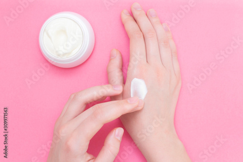 Hands of a beautiful well-groomed woman with a cream jar on a pink textural background. Moisturizer for clean and soft skin in the winter. I love the body. Healthcare concept.