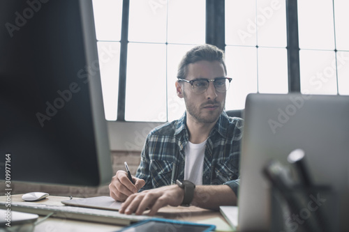 Young bearded man in eyeglasses drafting schemes