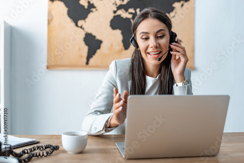 attractive travel agent in headset working near laptop