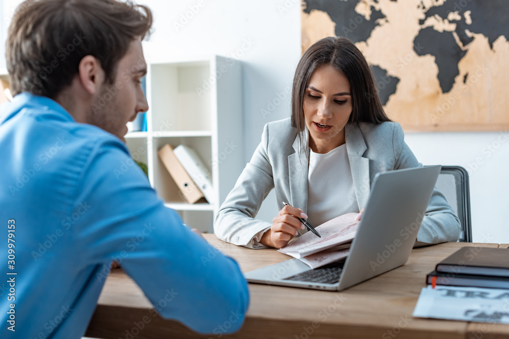 attractive travel agent pointing with pen at map while talking to client attractive travel agent pointing with pen at map while talking to client