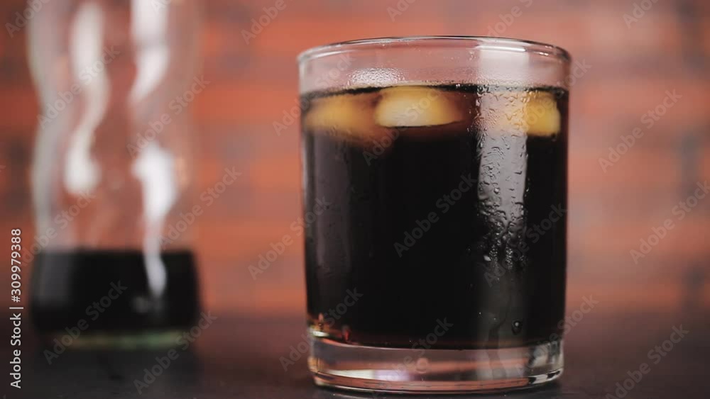 Ice cubes circling in the drinking glass with carbonated soda water, close-up view on brick wall background Ice cubes circling in the drinking glass with carbonated soda water, close-up view on brick wall background