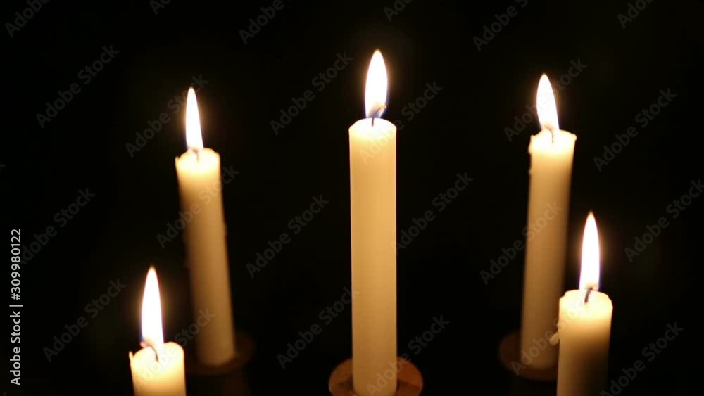 Five burning candles in a candlestick. Candles in a wooden candlestick burn night on a black background.