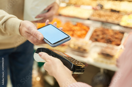 Close up of unrecognizable man paying via NFC while grocery shopping at farmers market, copy space