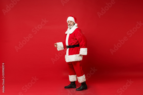 Side view of elderly gray-haired mustache bearded Santa man in Christmas hat posing isolated on red background. Happy New Year 2020 celebration holiday concept. Mock up copy space. Looking camera.