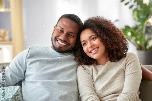 relations and people concept - happy african american couple sitting on sofa at home