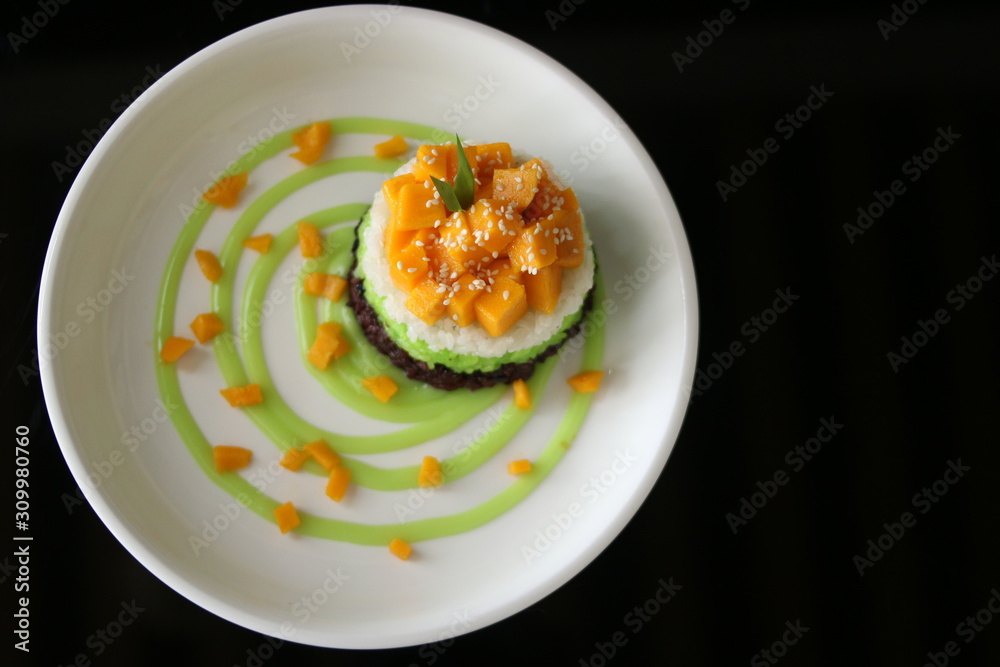 Delicious rice cake with manggo slice and sauce in black background