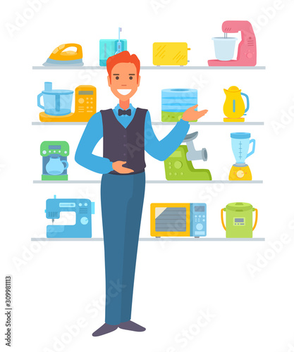 Consultant of the electronics store showing electric devices, pointing his palm to the side, looking at the viewer.
