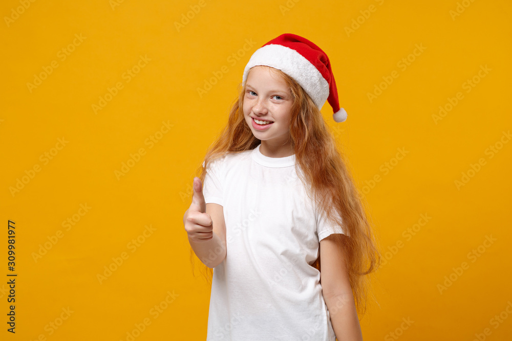 Cute little ginger kid Santa girl 12-13 years old in white t-shirt, Christmas hat isolated on yellow background. Happy New Year 2020 celebration holiday concept. Mock up copy space. Showing thumb up. Cute little ginger kid Santa girl 12-13 years old in white t-shirt, Christmas hat isolated on yellow background. Happy New Year 2020 celebration holiday concept. Mock up copy space. Showing thumb up.
