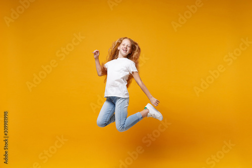 Cheerful little ginger kid girl 12-13 years old in white t-shirt isolated on yellow background children portrait. Childhood lifestyle concept. Mock up copy space. Having fun, fooling around, jumping.