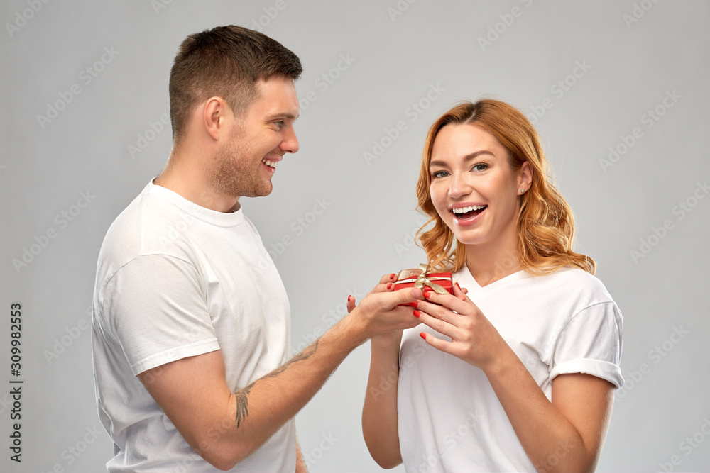 relationships, holiday and valentines day concept - happy couple in white t-shirts with christmas gift over grey background relationships, holiday and valentines day concept - happy couple in white t-shirts with christmas gift over grey background