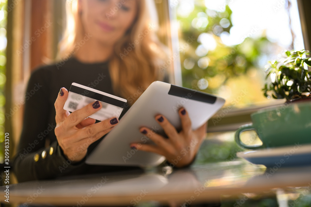 Pretty blond woman online shopping on her tablet by the window in a coffee shop. Pretty blond woman online shopping on her tablet by the window in a coffee shop.