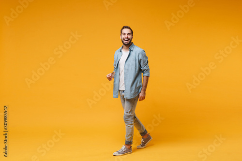 Funny laughing young bearded man in casual blue shirt posing isolated on yellow orange wall background, studio portrait. People sincere emotions lifestyle concept. Mock up copy space. Looking camera.