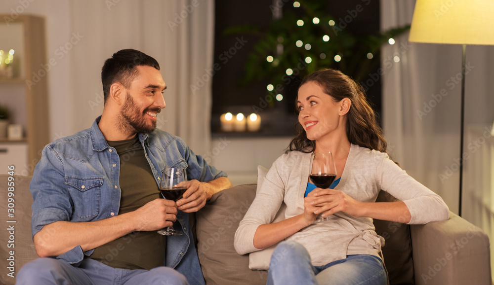 leisure, clebration and valentines day concept - happy couple drinking red wine at home in evening