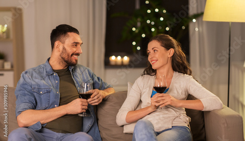 leisure, clebration and valentines day concept - happy couple drinking red wine at home in evening photo
