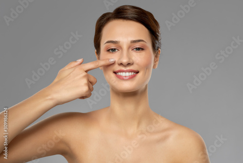 beauty, bodycare and people concept - smiling beautiful young woman showing her nose over grey background
