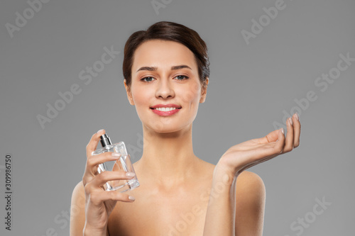 perfumery, beauty and luxury concept - happy smiling young woman with perfume over grey background