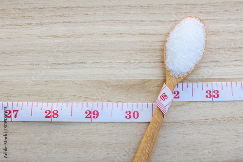Sugar in  spoon and measuring tape  on a wooden background.