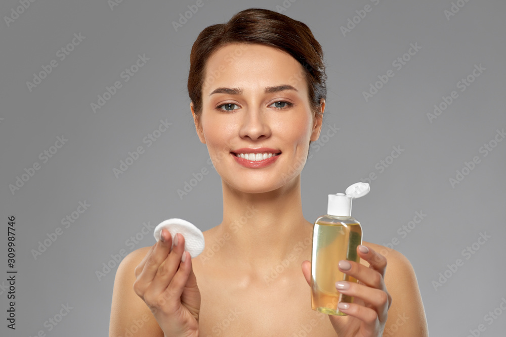 beauty, skin care and people concept - smiling young woman with toner or cleanser and cotton pad over grey background beauty, skin care and people concept - smiling young woman with toner or cleanser and cotton pad over grey background