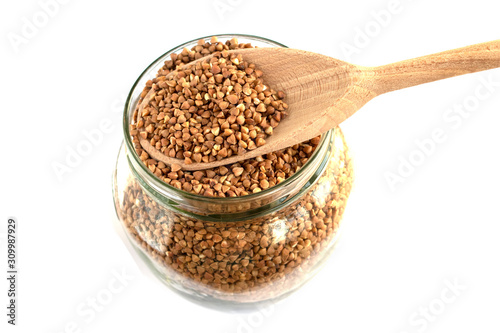 glass jar with buckwheat and a wooden spoon on white isolate background
