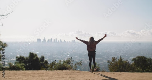 A young woman walking to the edge of a cliff with a view of the city of Los Angeles.