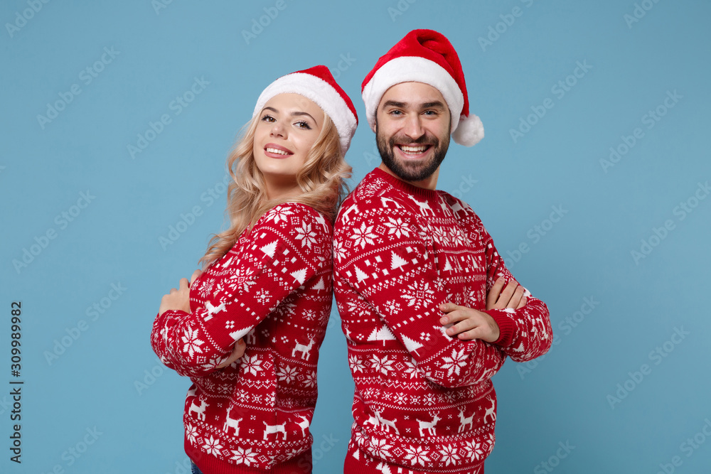 Smiling young couple guy girl in Christmas sweaters, Santa hat posing isolated on blue background. Happy New Year 2020 celebration holiday party concept. Mock up copy space. Holding hands crossed. Smiling young couple guy girl in Christmas sweaters, Santa hat posing isolated on blue background. Happy New Year 2020 celebration holiday party concept. Mock up copy space. Holding hands crossed.