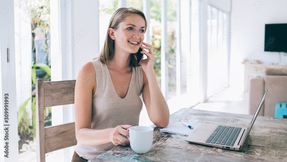 Delighted female sitting at desk and chatting by mobile Delighted female sitting at desk and chatting by mobile