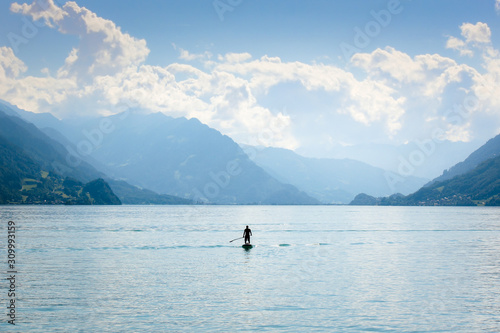 Silhouette of a man standing on a paddleboard on Lake Brienz in Switzerland. Hills in the background. Active lifestyle, sport activities. Peaceful background, motivational concept