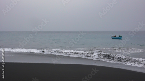 African fisherman in a wooden skiff fishing on the black lava sand coast of Fogo Island in Cape Verde photo