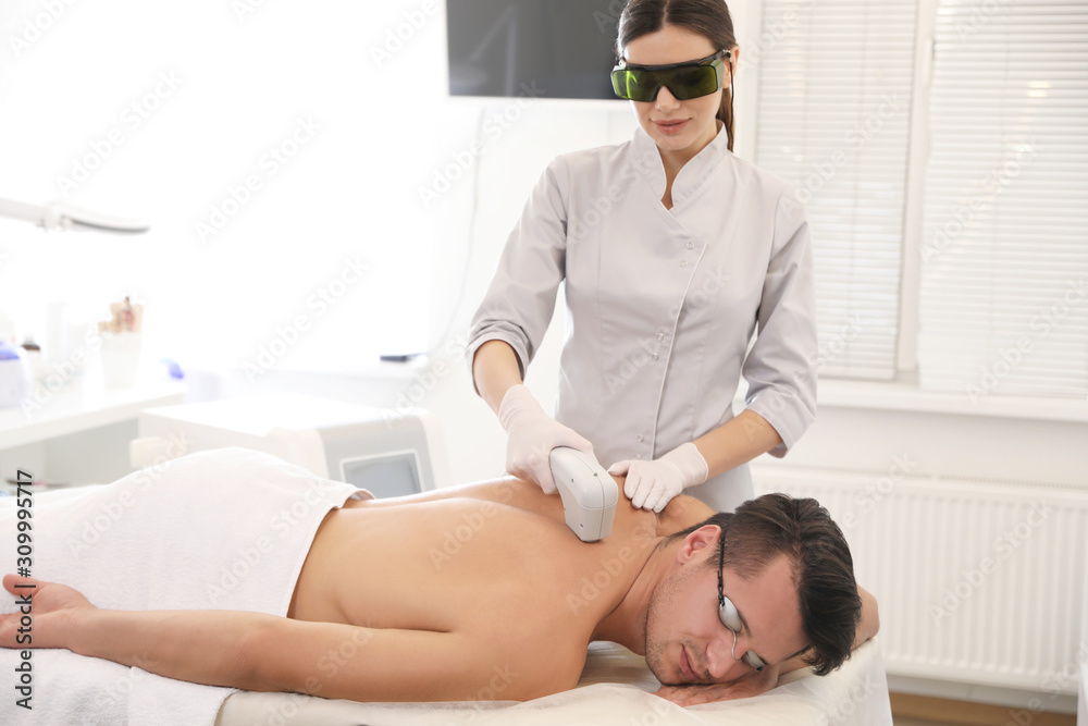 Fototapeta premium Young man undergoing laser epilation procedure in beauty salon