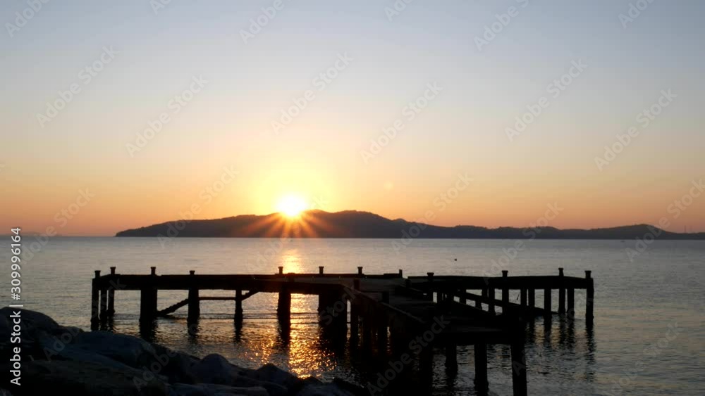 The sunrise behind the mountains in the sea at the old pier The sunrise behind the mountains in the sea at the old pier
