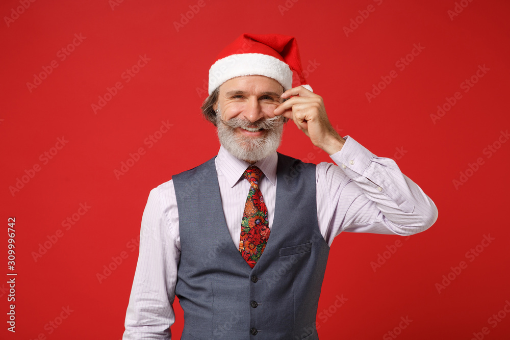 Smiling elderly gray-haired mustache bearded Santa man in Christmas hat shirt vest tie isolated on red background. New Year 2020 celebration holiday concept. Mock up copy space. Keeping hand on cheek. Smiling elderly gray-haired mustache bearded Santa man in Christmas hat shirt vest tie isolated on red background. New Year 2020 celebration holiday concept. Mock up copy space. Keeping hand on cheek.