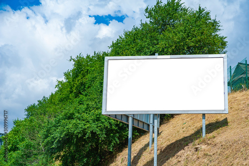 Blank white advertising billboard on the hillside in the city. Sunny summer day with blue sky.