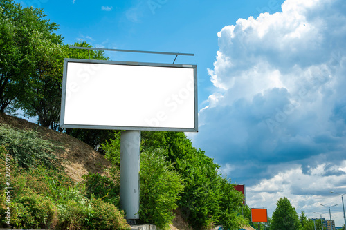 Blank white advertising billboard on the hillside in the city. Sunny summer day with blue sky.