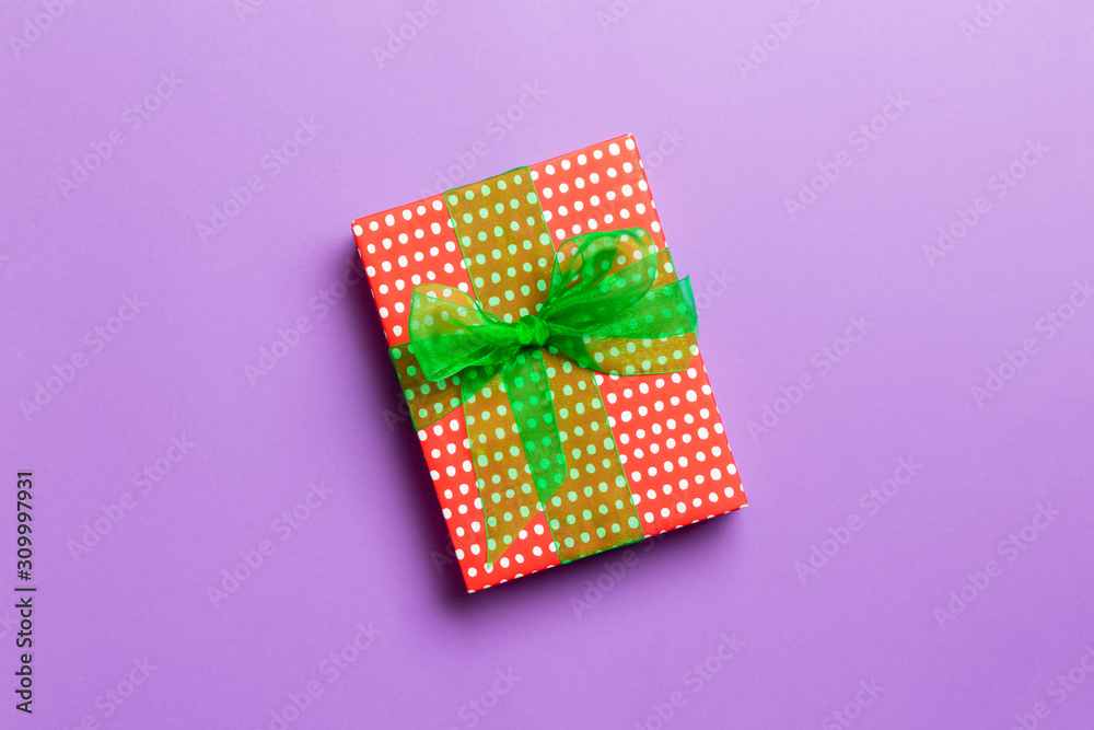 wrapped Christmas or other holiday handmade present in paper with green ribbon on purple background. Present box, decoration of gift on colored table, top view with copy space wrapped Christmas or other holiday handmade present in paper with green ribbon on purple background. Present box, decoration of gift on colored table, top view with copy space