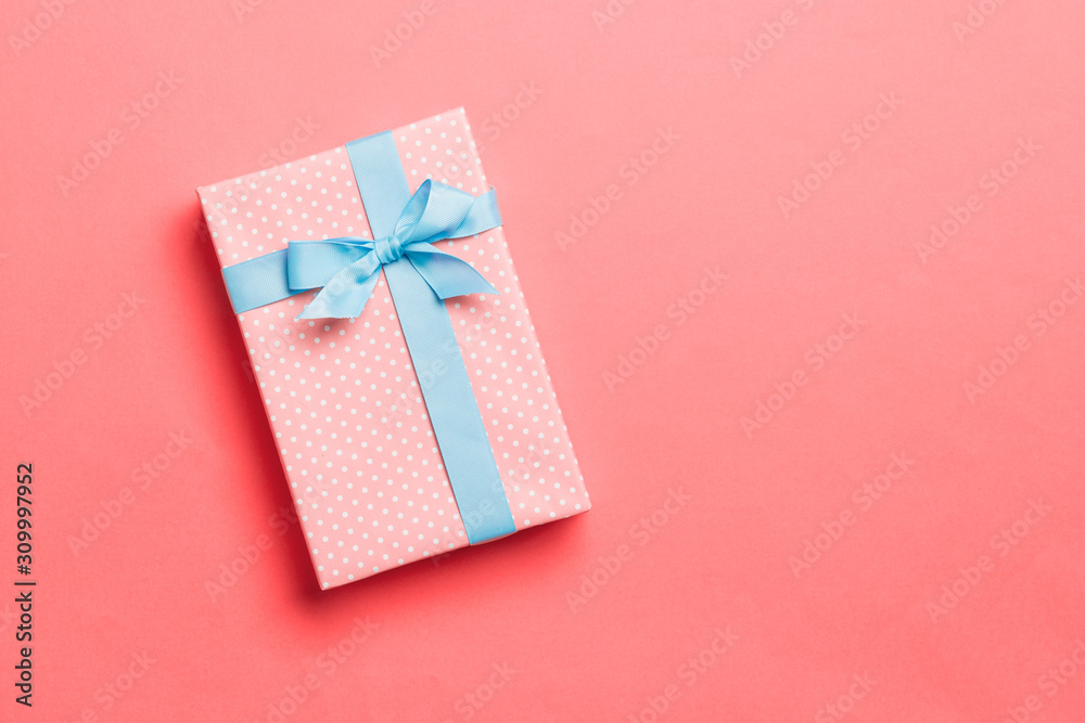 Top view Christmas present box with blue bow on living coral background with copy space Top view Christmas present box with blue bow on living coral background with copy space