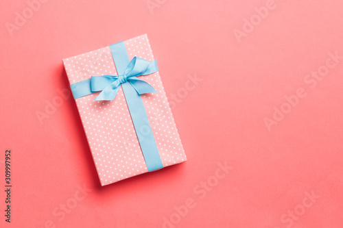 Top view Christmas present box with blue bow on living coral background with copy space
