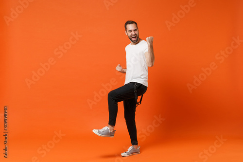 Overjoyed happy young man in casual white t-shirt posing isolated on bright orange wall background studio portrait. People sincere emotions lifestyle concept. Mock up copy space. Doing winner gesture. © ViDi Studio