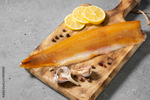 Cold smoked muksun fish on a wooden Board on a gray kitchen table. Whole fillet of fish whitefish or muksun closeup. Top view with space for text photo