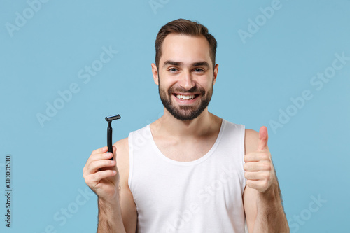 Bearded man 20s years old in white shirt hold one-off disposable plastic razor isolated on blue pastel background studio portrait. Skin care healthcare cosmetic procedures concept. Mock up copy space.