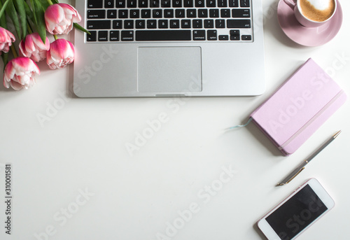 Home office desk in pink colors with laptop, cup of coffee, rose notebook, phone, pink tulips on a white background. Flat lay Business womans workplace and objects. Top view. Copy space for text