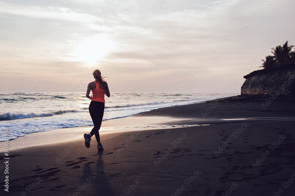 Young woman jogging on sea beach at sunny day