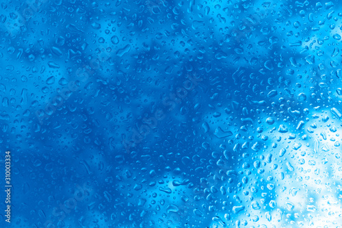 Large drops of water on the glass. Raindrops on the glass against the background of the blue sky. Copy space. Trendy color 2020. Classic blue background.