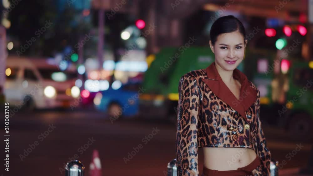 Sexy and alluring Asian woman flirts with the camera on the city at night with traffic moving by in the background Sexy and alluring Asian woman flirts with the camera on the city at night with traffic moving by in the background
