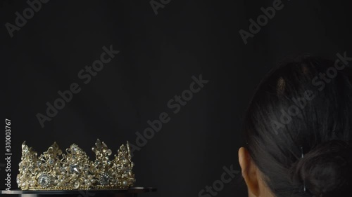 Beauty pageant queen or bride places a diamond, pearl and silver crown on her head - black background photo