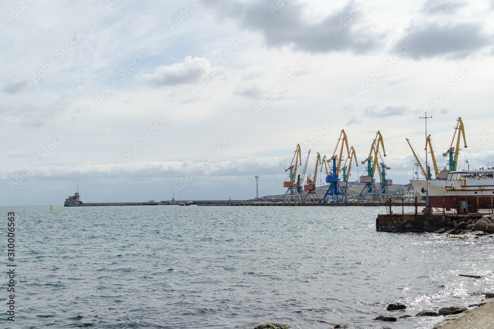 Cargo port of Feodosia with cranes and ships. View from from the city promenade. Feodosia, Crimea, Russia - September 26, 2019