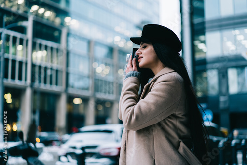 Inspired woman in coat and hat taking photo with camera