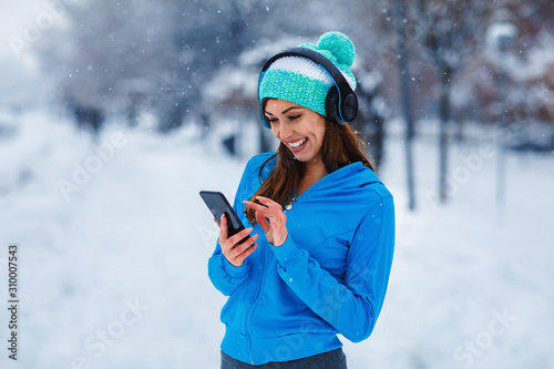 Young sports woman enjoys music after jogging  on snowy day in the city