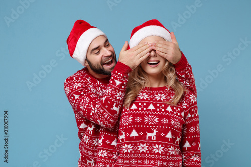 Funny young couple guy girl in Christmas sweaters, Santa hat posing isolated on blue background. Happy New Year 2020 celebration holiday party concept. Mock up copy space. Covering eyes with hands.